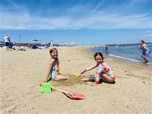 Two young girls joyfully playing in sand on a sunny beach, building castles & enjoying their day.