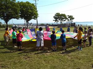 A group of children joyfully gathered around a large, colorful kite on a sunny day.