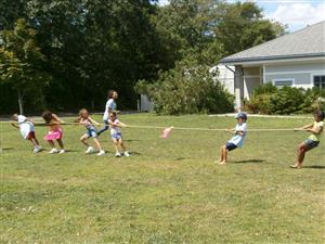 A group of children joyfully playing tug of war in a sunny yard, showcasing teamwork and fun.