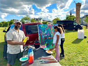 A man creates art on a table, accompanied by two people who are attentively painting.