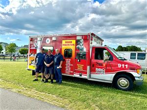 Three men stand beside an ambulance truck, ready for action in a medical emergency situation.